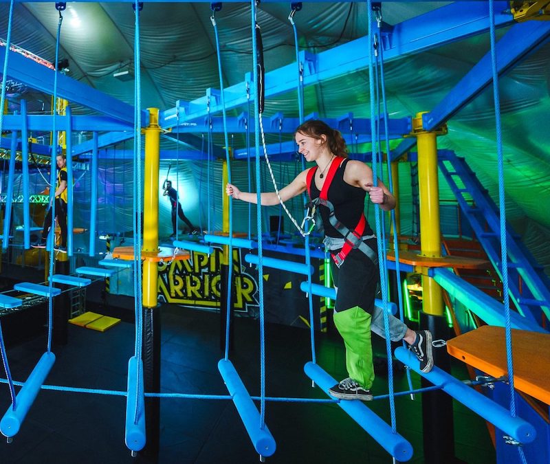 Junge Frau beim Klettern im Indoor-Hochseilgarten bei Jumpin Warrior