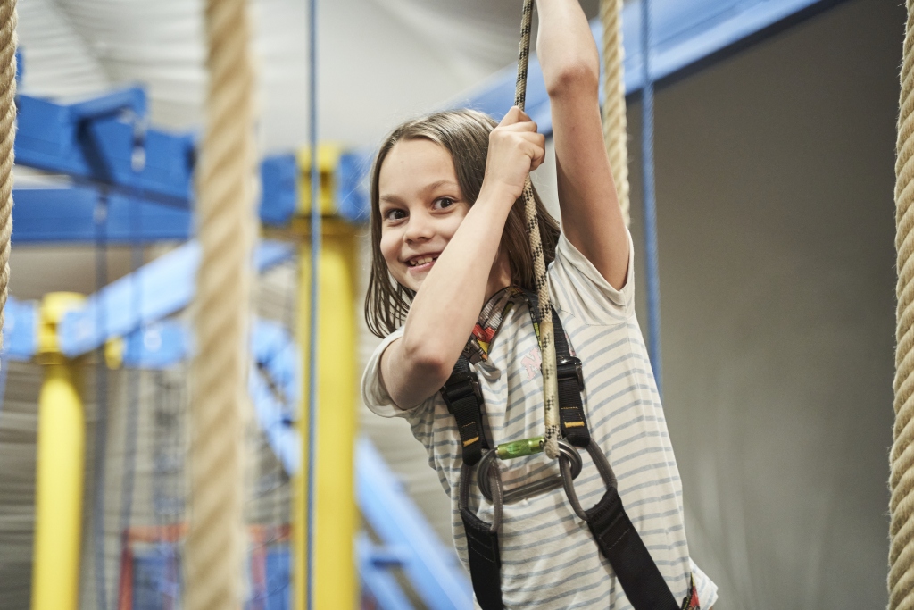 Mädchen mit Sicherungsseil im Hochseilgarten des Jumpin Warrior Indoor Abenteuerparks