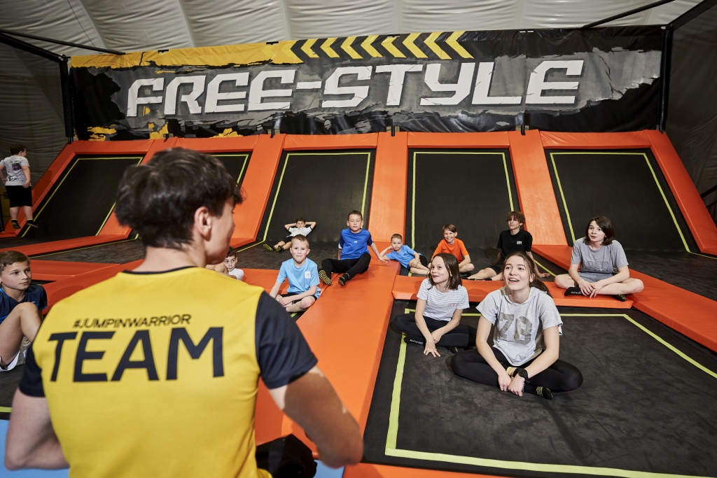 Kinder sitzen um einen Trainer im Trampolinbereich beim Jumpin Warrior Freestyle